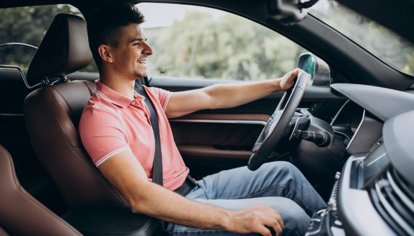 conducteur souriant la main sur le volant et l'autre sur le pommeau de vitesse